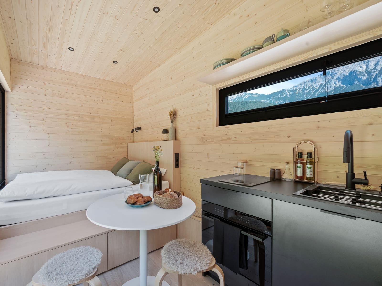 Innenraum mit Bett, Tisch und Küchenzeile vor dem Panoramafenster